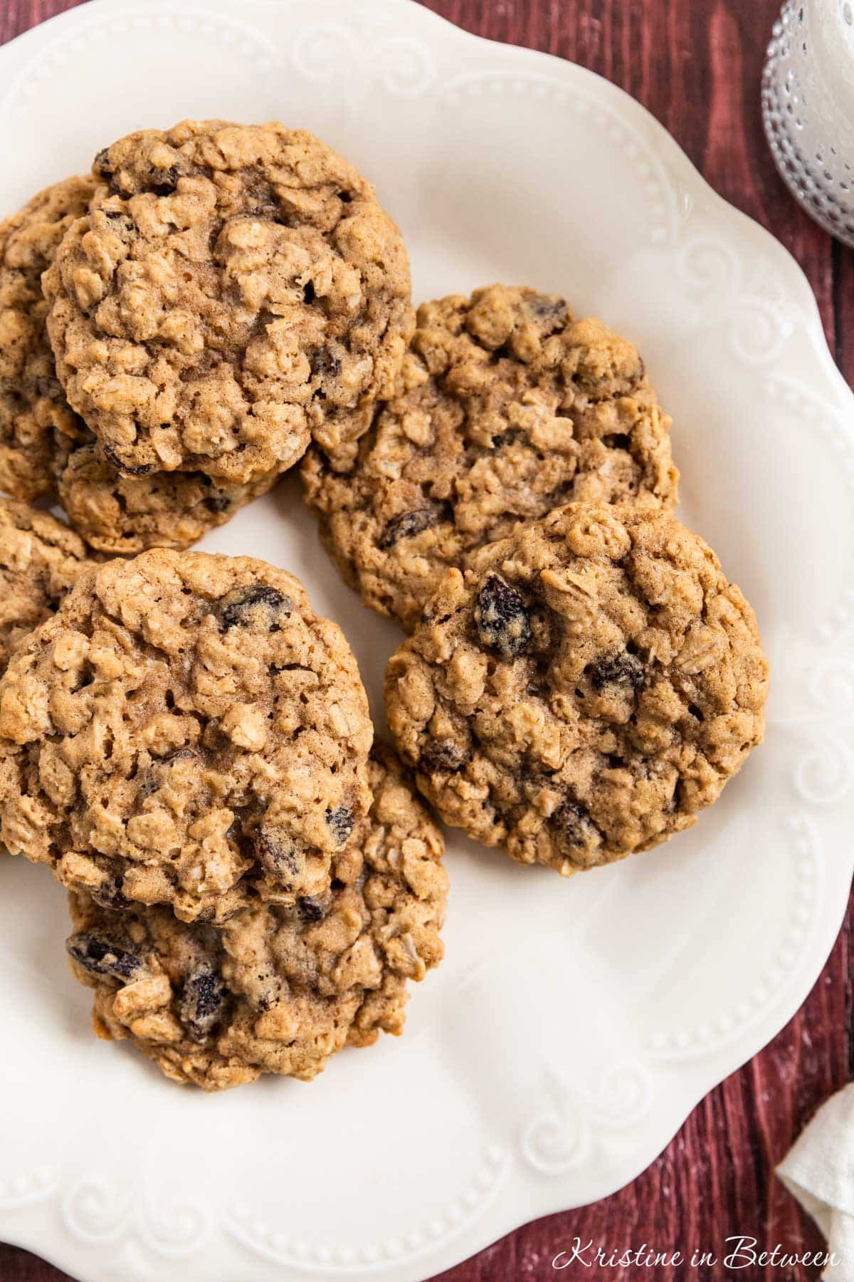 Old-fashioned oatmeal raisin cookies stacked upon a white plate with one broken in half to show the inside.