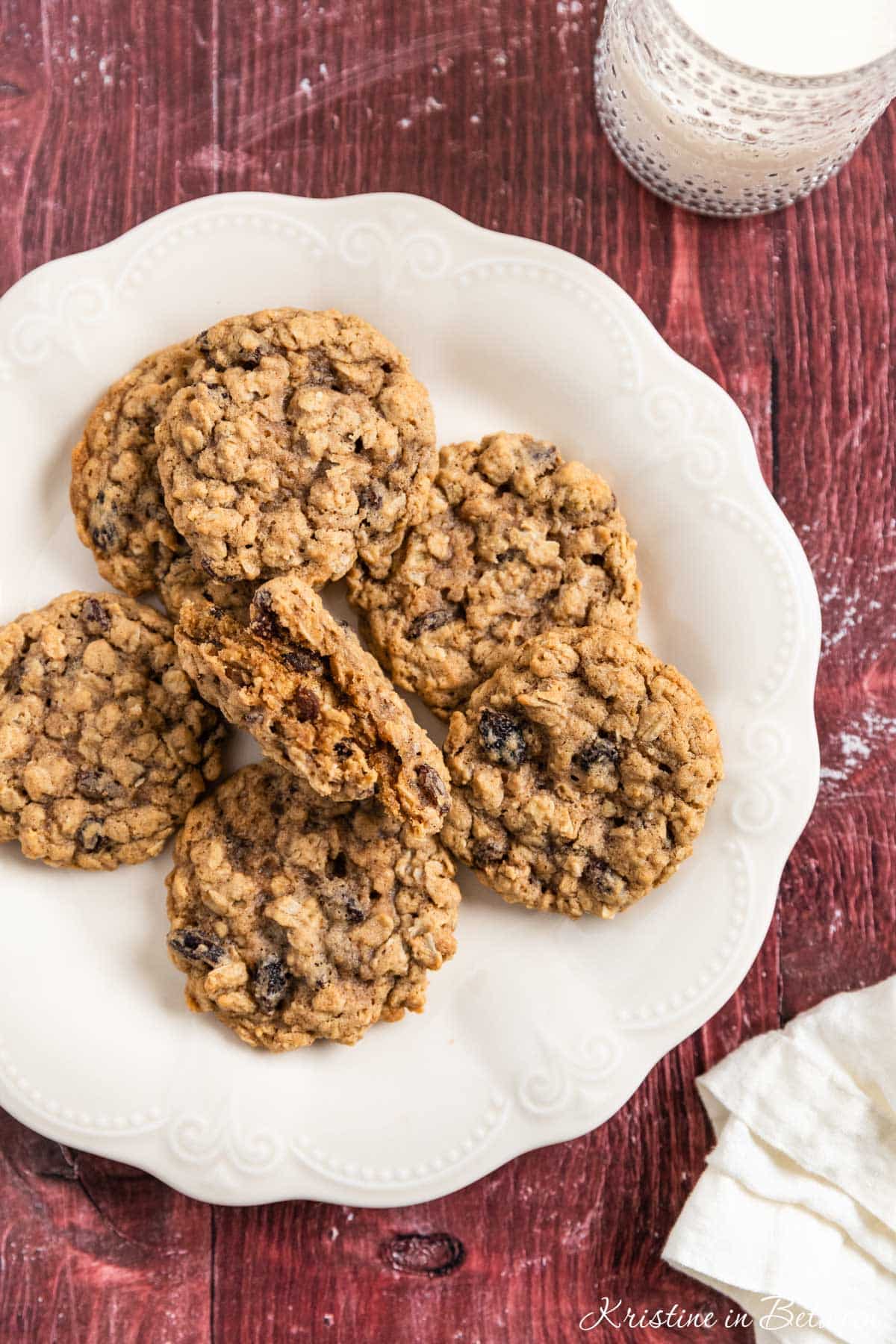 Old-fashioned oatmeal raisin cookies stacked upon a white plate with one broken in half to show the inside.