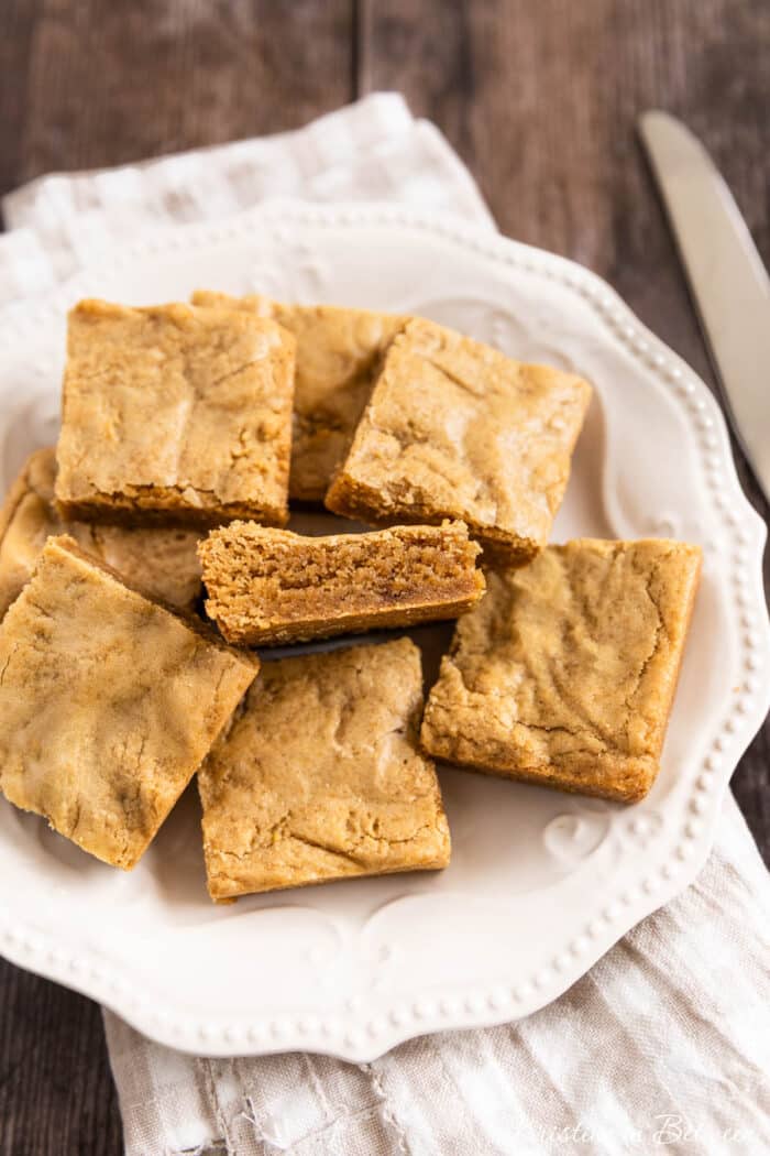 Small-batch blondies cut into squares on a white plate with a knife next to them.