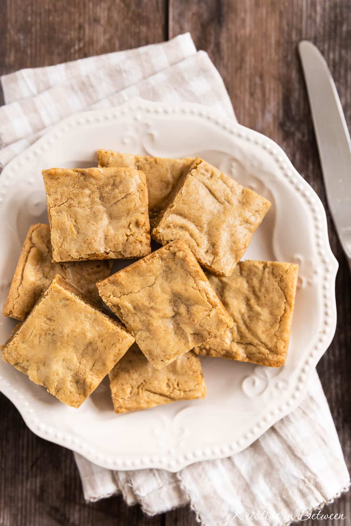 Small-batch blondies cut into squares on a white plate with a knife next to them.