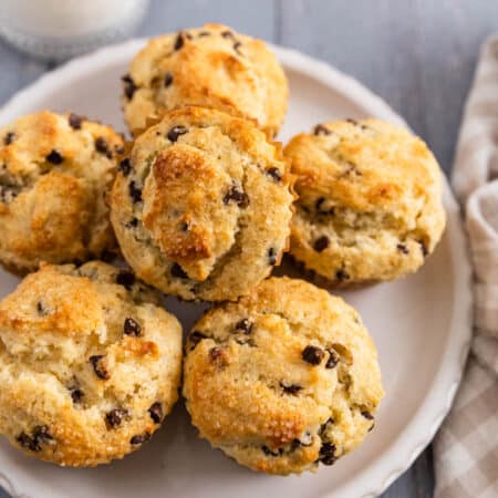 A plate of small batch chocolate chip muffins with a glass of milk next to it.