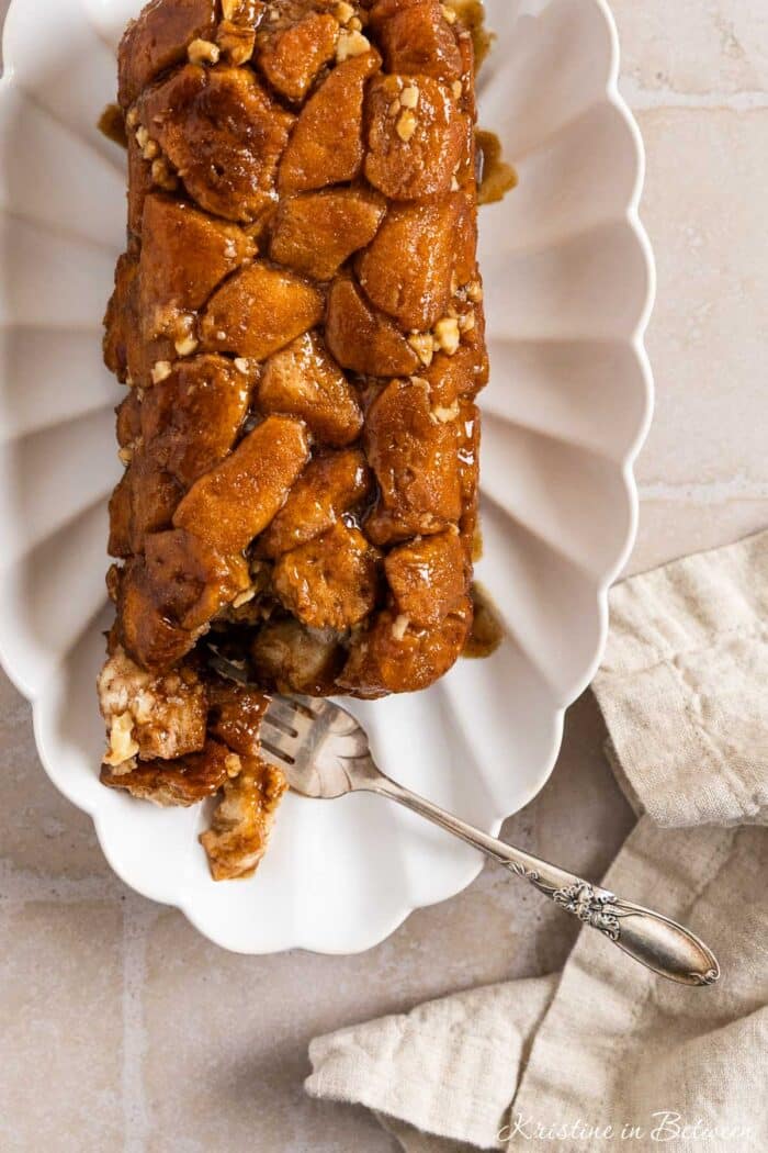 Monkey bread on a white plate with a bite on a fork and a napkin next to it.