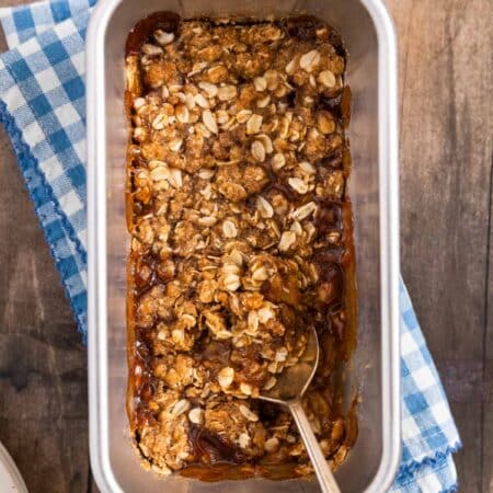 Small-batch peach crumble in a loaf pan with a spoon in it.