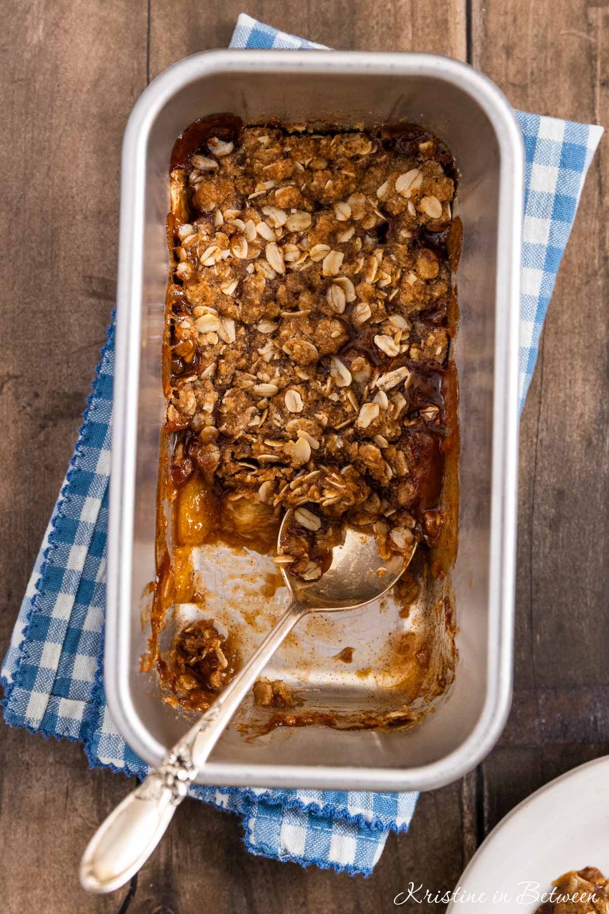 Small-batch peach crumble in a loaf pan with a spoon in it.