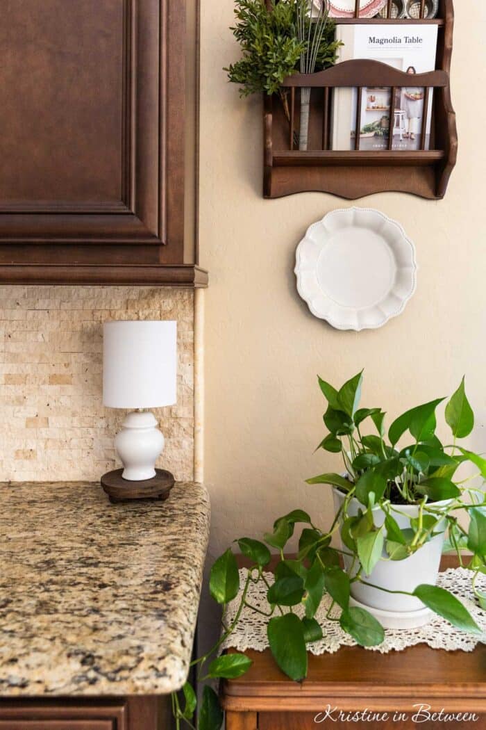 A cottage kitchen with a white lamp and a green plant sitting on a doily.
