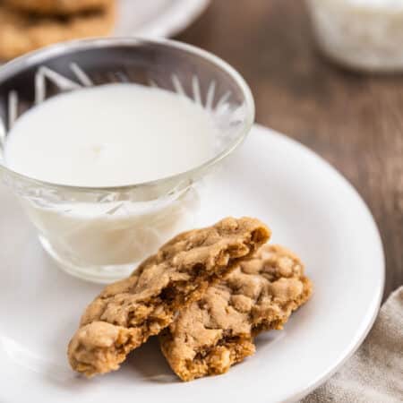 A plate of oatmeal cookies with a cup of milk and a tan napkin next to it.