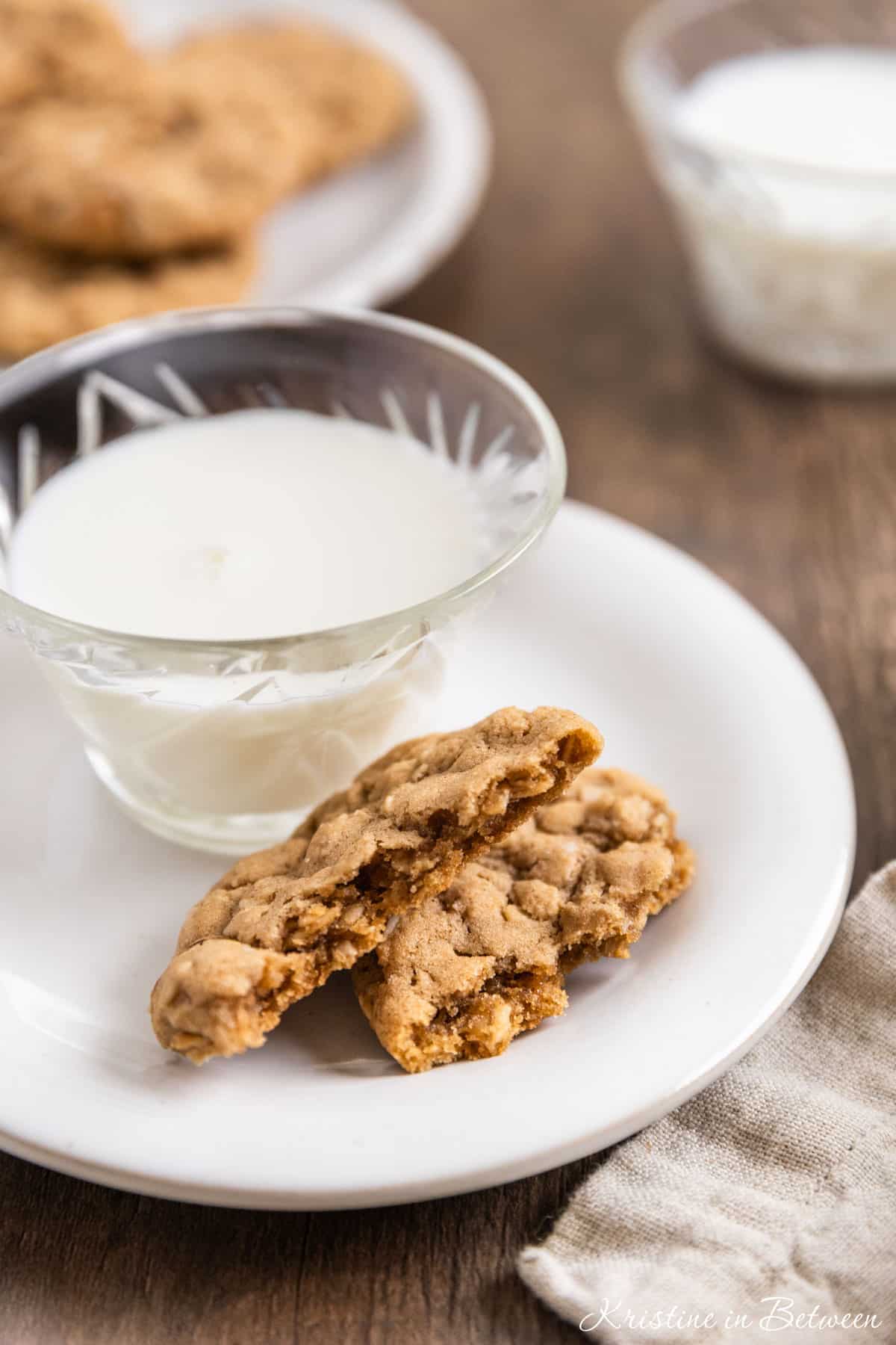 A plate of oatmeal cookies with a cup of milk and a tan napkin next to it.