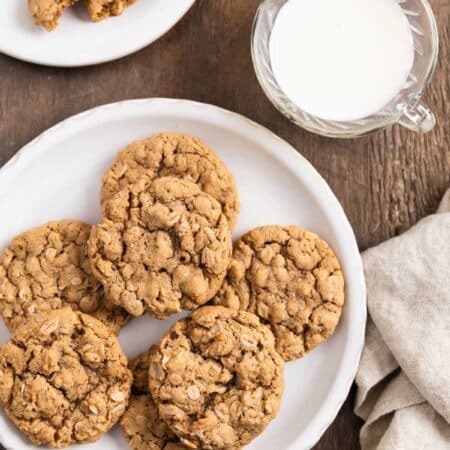 A plate of oatmeal cookies with a cup of milk and a tan napkin next to it.