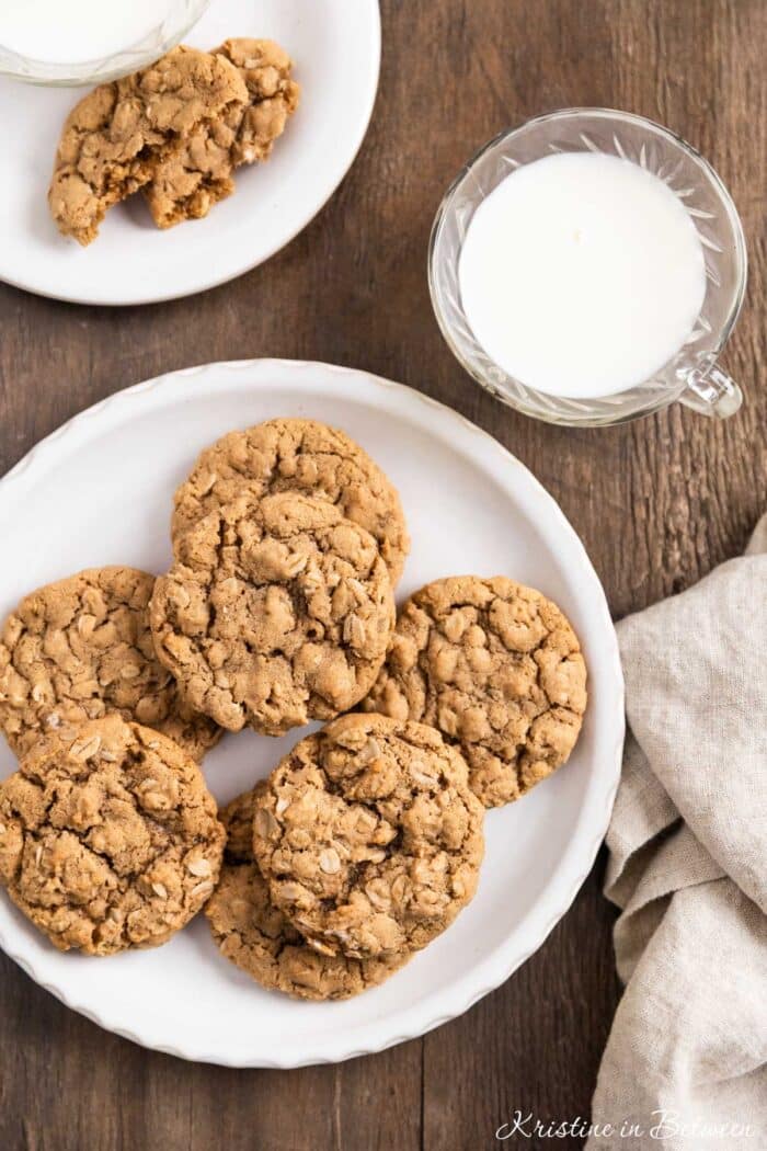 A plate of oatmeal cookies with a cup of milk and a tan napkin next to it.