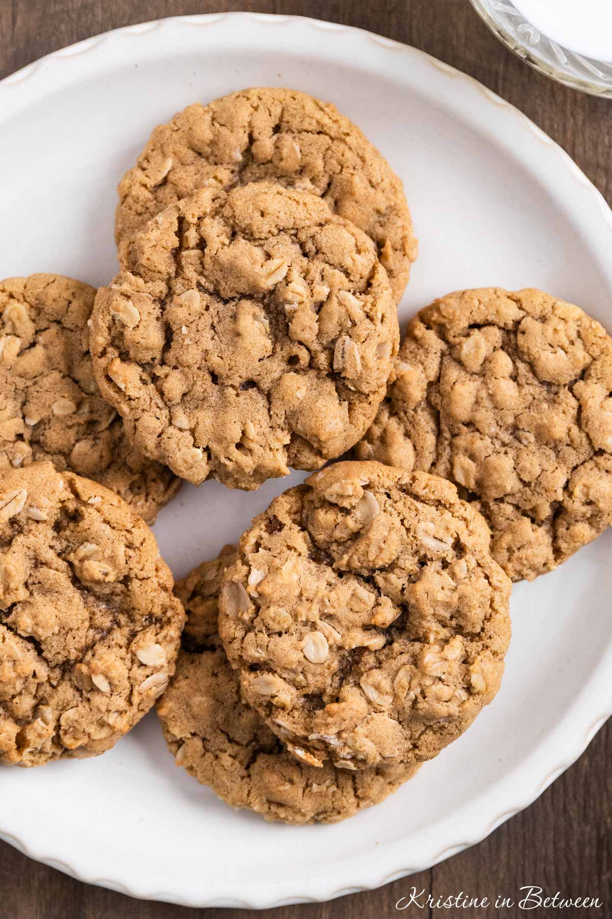A plate of oatmeal cookies with a cup of milk and a tan napkin next to it.