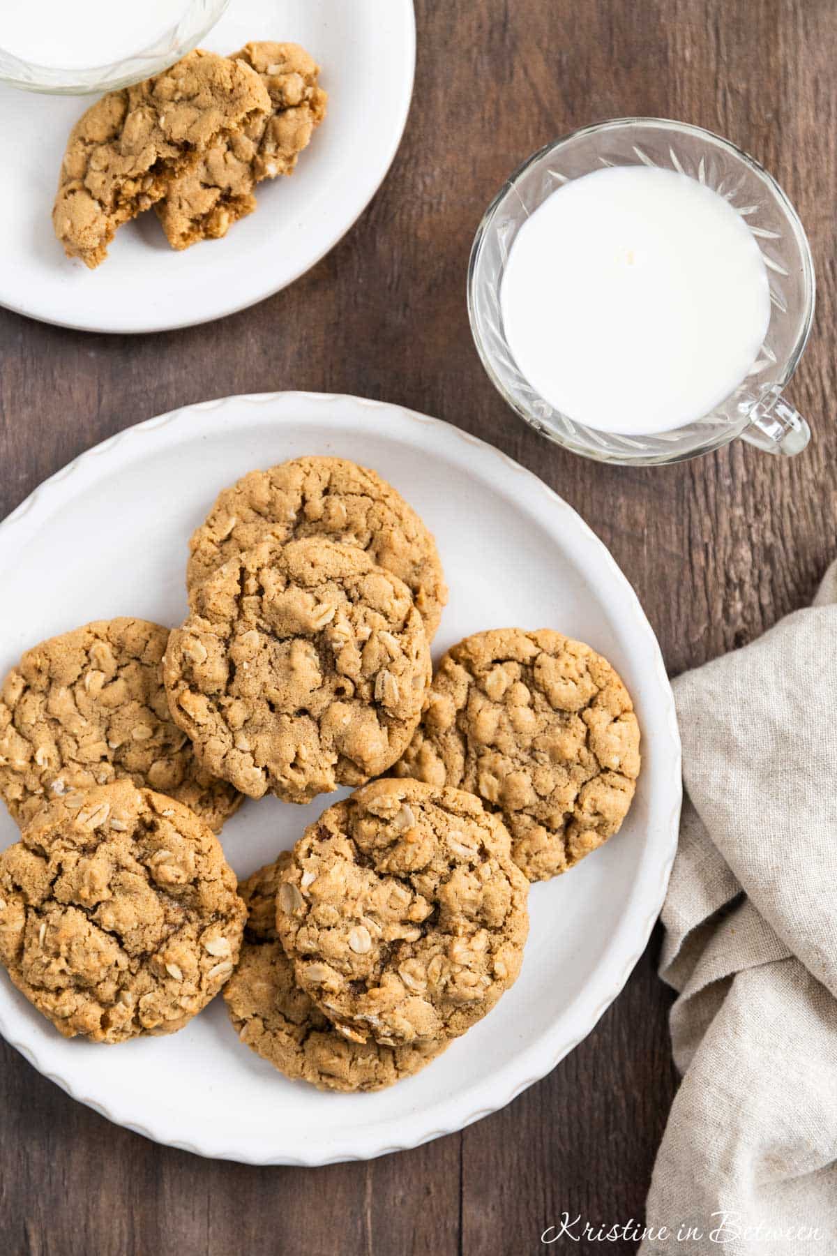 A plate of oatmeal cookies with a cup of milk and a tan napkin next to it.