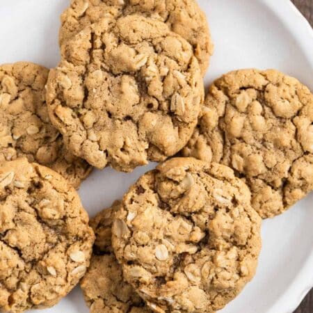 A plate of oatmeal cookies with a cup of milk and a tan napkin next to it.