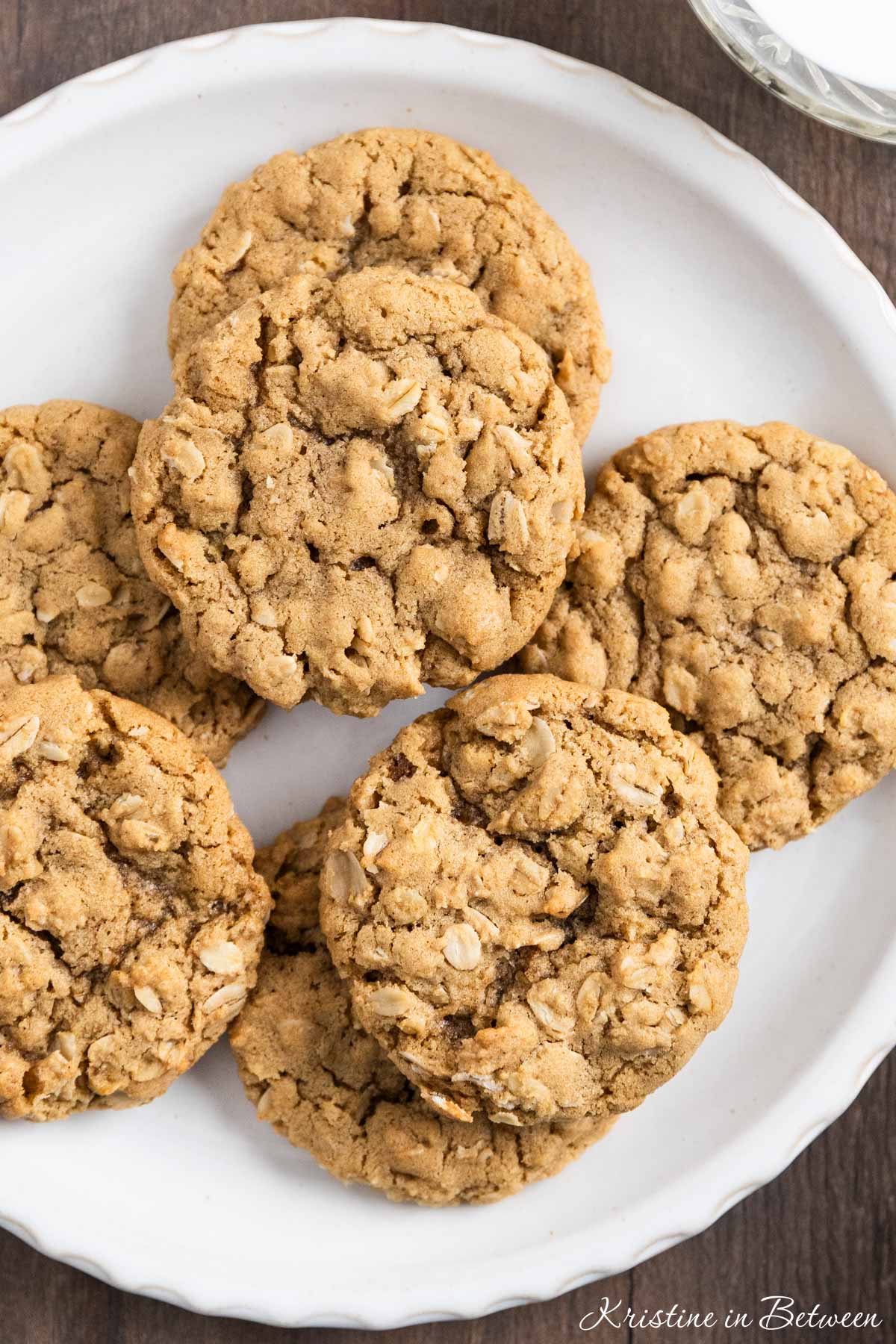 A plate of oatmeal cookies with a cup of milk and a tan napkin next to it.