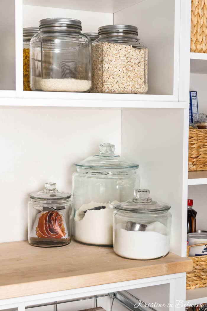 Several different glass jars and canisters with pantry ingredients in them.