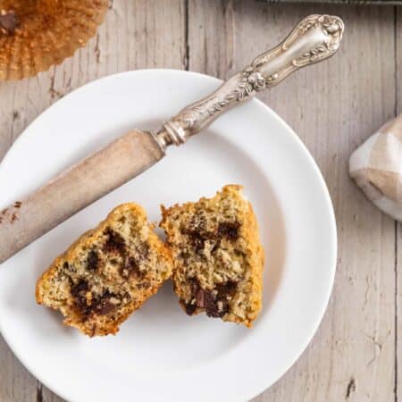 A muffin on a white plate that's cut in half with a knife next to it.