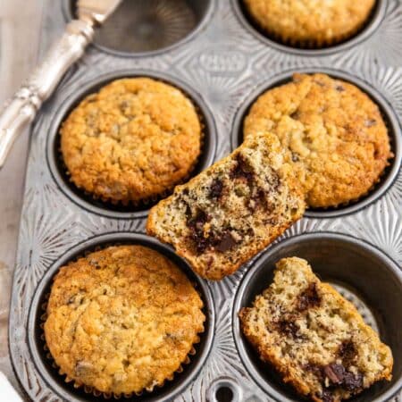 A tin of banana muffins with a knife sitting next to them.