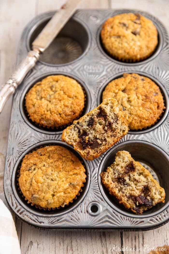 A tin of banana muffins with a knife sitting next to them.