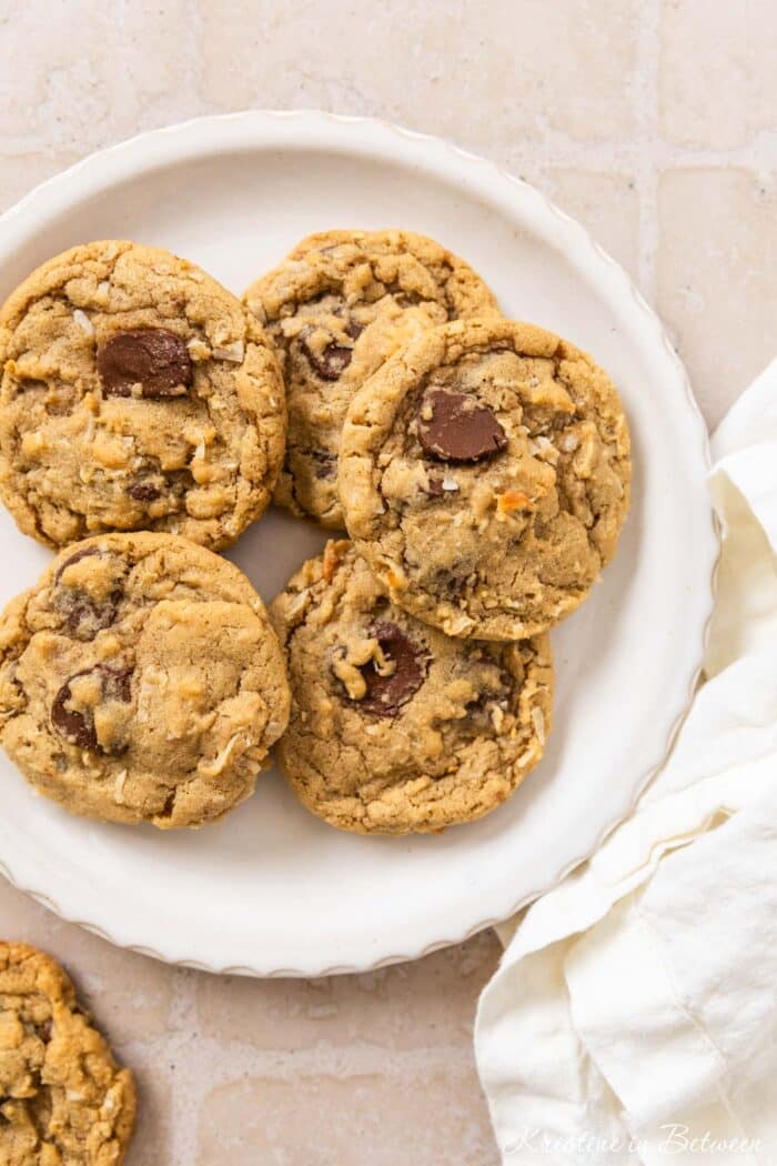 A plate of chocolate chip coconut cookies with a white napkin laying next to them.