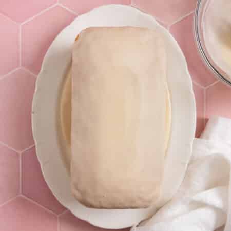 A loaf of vanilla cake with glaze on top and a white napkin sitting next to it.