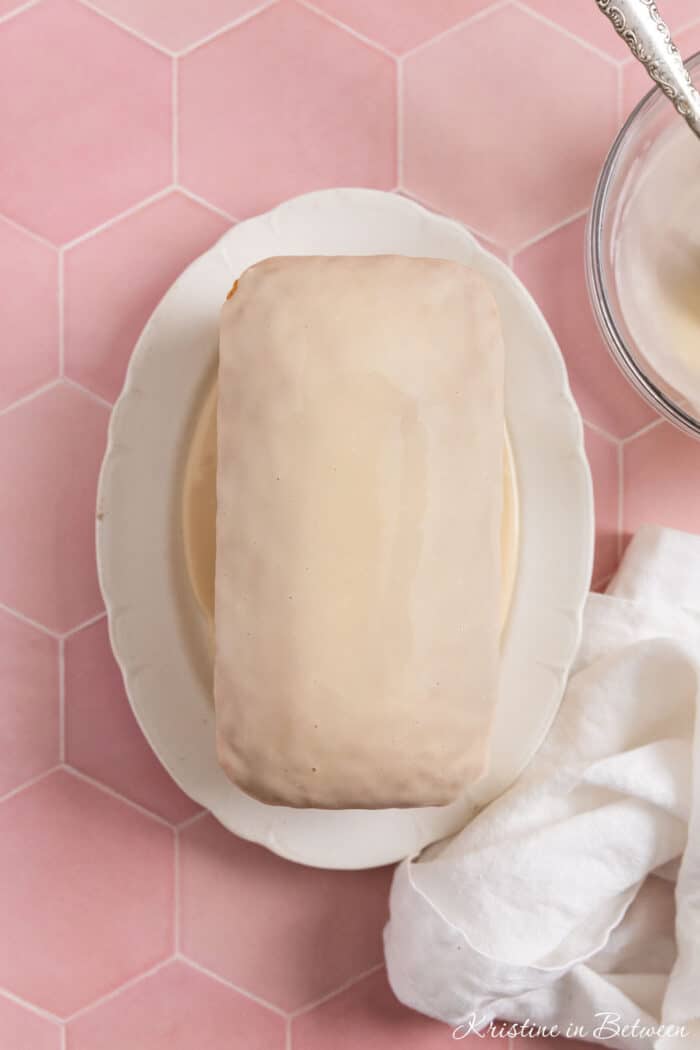 A loaf of vanilla cake with glaze on top and a white napkin sitting next to it.