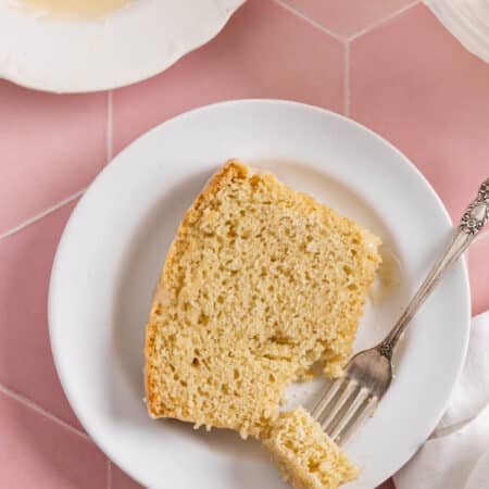 A slice of vanilla cake on a white plate with a bite on a fork.