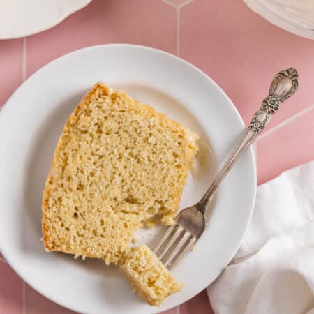 A slice of vanilla cake on a white plate with a bite on a fork.