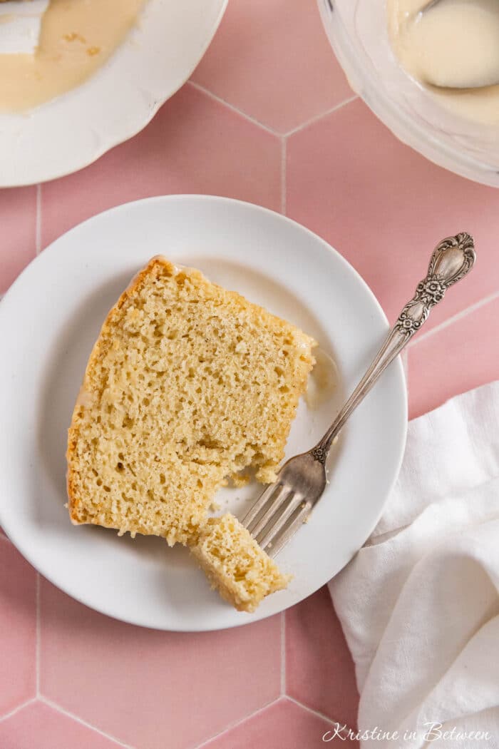 A slice of vanilla cake on a white plate with a bite on a fork.