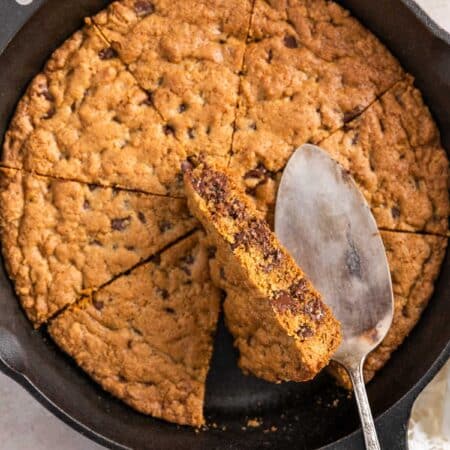 A skillet cookie in a cast iron pan with an antique spatula sitting on top.