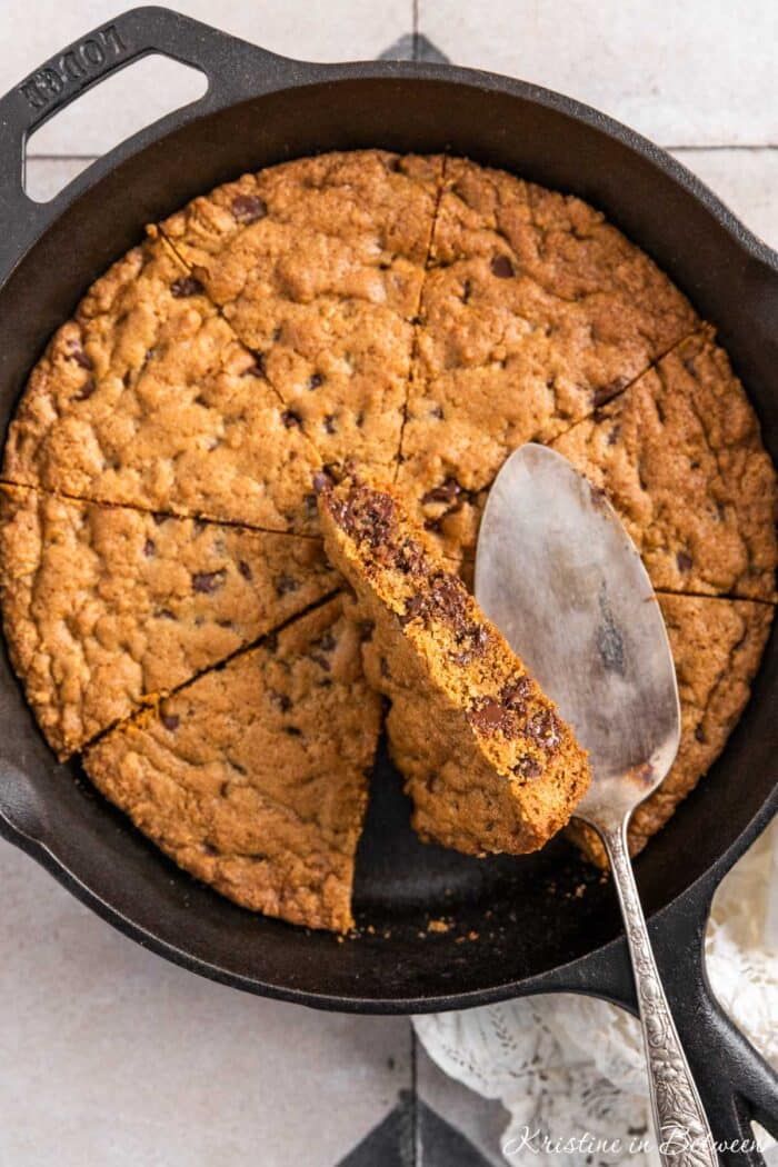 A skillet cookie in a cast iron pan with an antique spatula sitting on top.