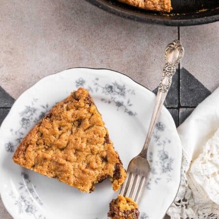 A piece of skillet cookie on a plate with a bite on a fork and the rest of the cookie in the background.