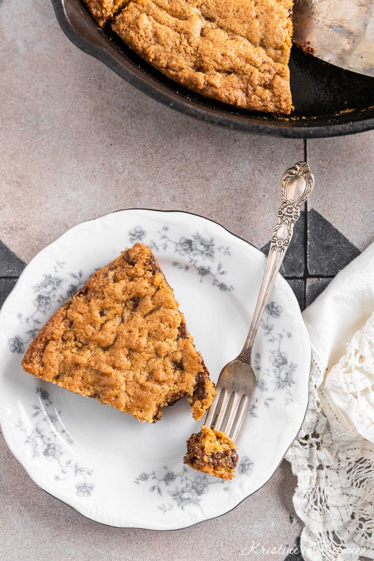 A piece of skillet cookie on a plate with a bite on a fork and the rest of the cookie in the background.