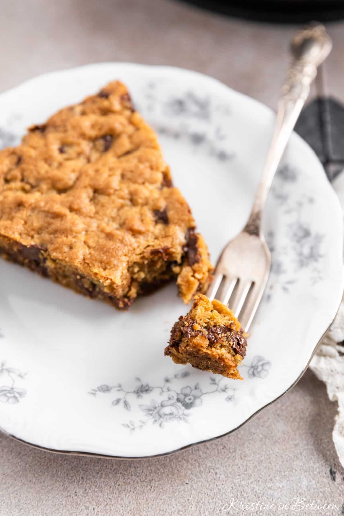 A slice of a skillet chocolate chip cookie on a white plate with a bite on a fork.
