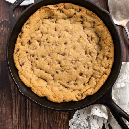 A skillet chocolate chip cookie in a cast iron pan with a spatula next to it.