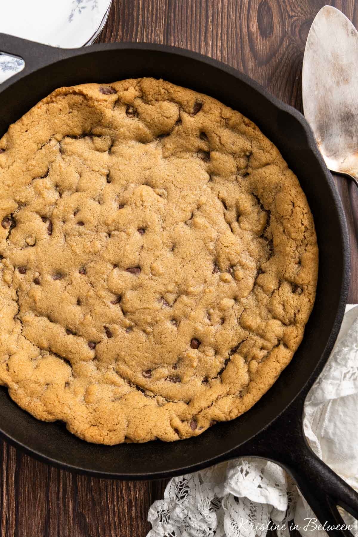 A skillet chocolate chip cookie in a cast iron pan with a spatula next to it.