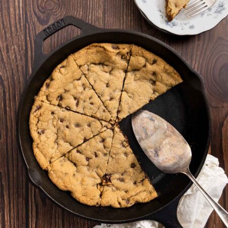 A skillet cookie sliced up with a piece on a spatula ready to be served.