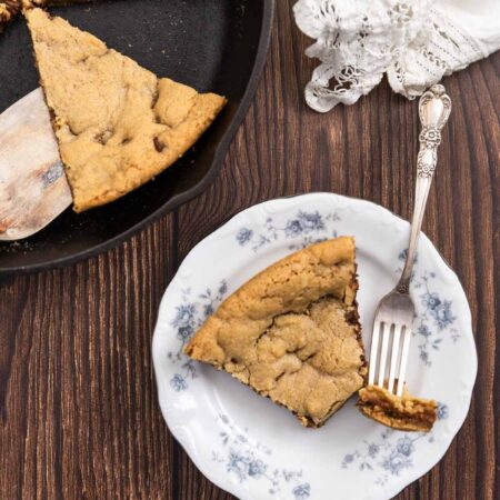 A bite of a skillet cookie on a fork with the rest of the slice on a plate.