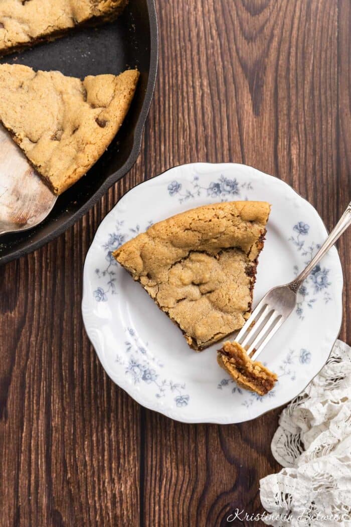 A bite of a skillet cookie on a fork with the rest of the slice on a plate.