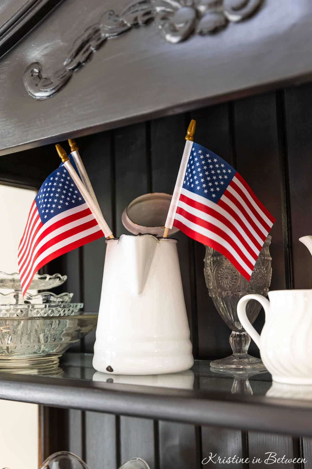 An enamel coated coffee pitcher with three flags in it.