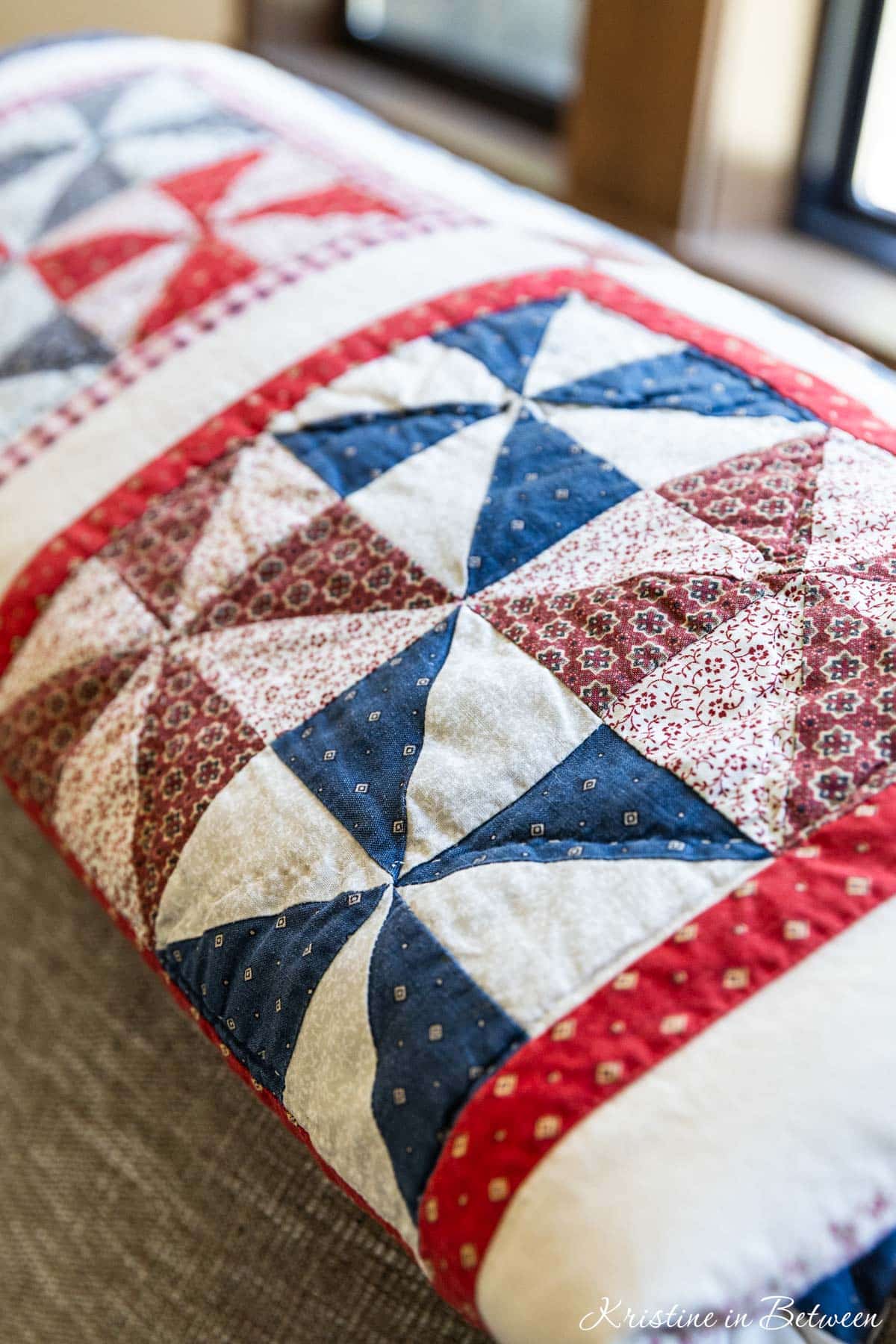 A red, white, and blue quilt on the back of a softa.