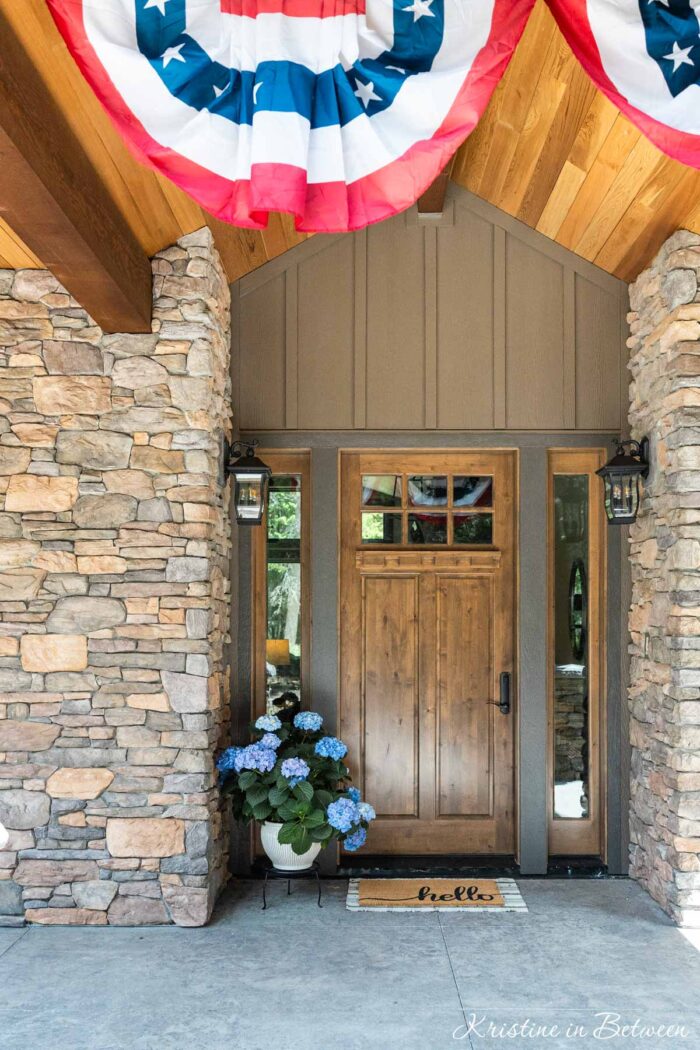 A front porch with bunting flags and a pot of blue hydrangeas in a pot.