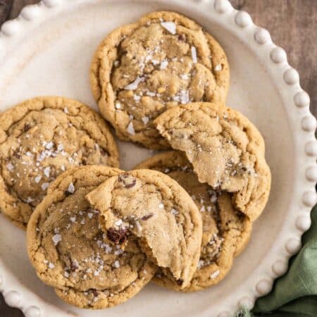 Chocolate chip cookies with sea salt sprinkled on top sitting on a white plate.