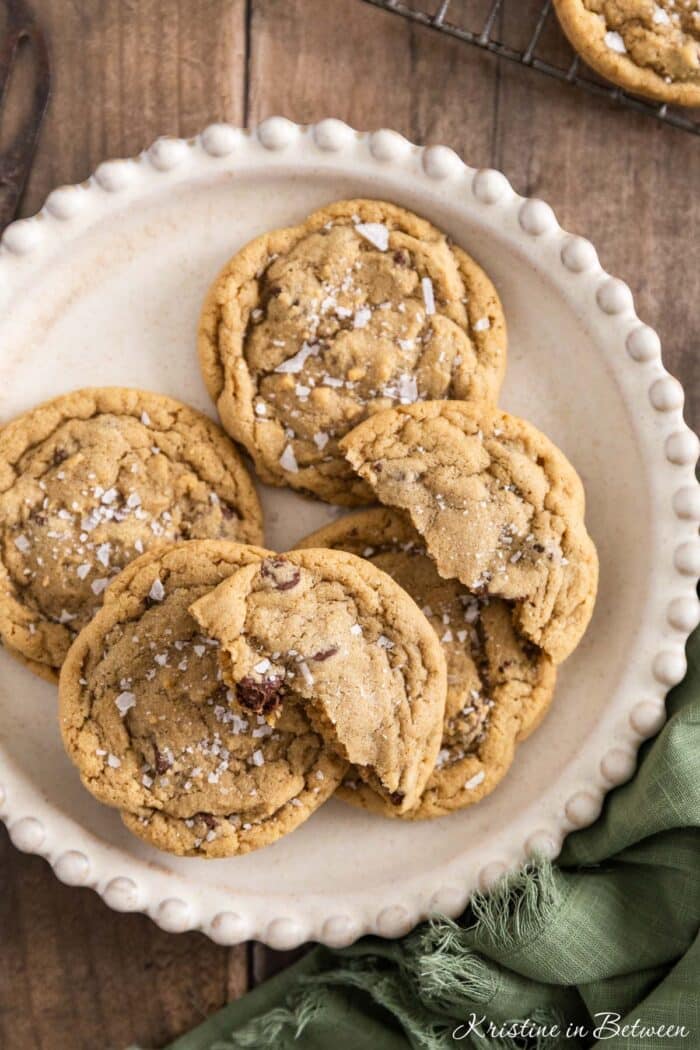 Chocolate chip cookies with sea salt sprinkled on top sitting on a white plate.