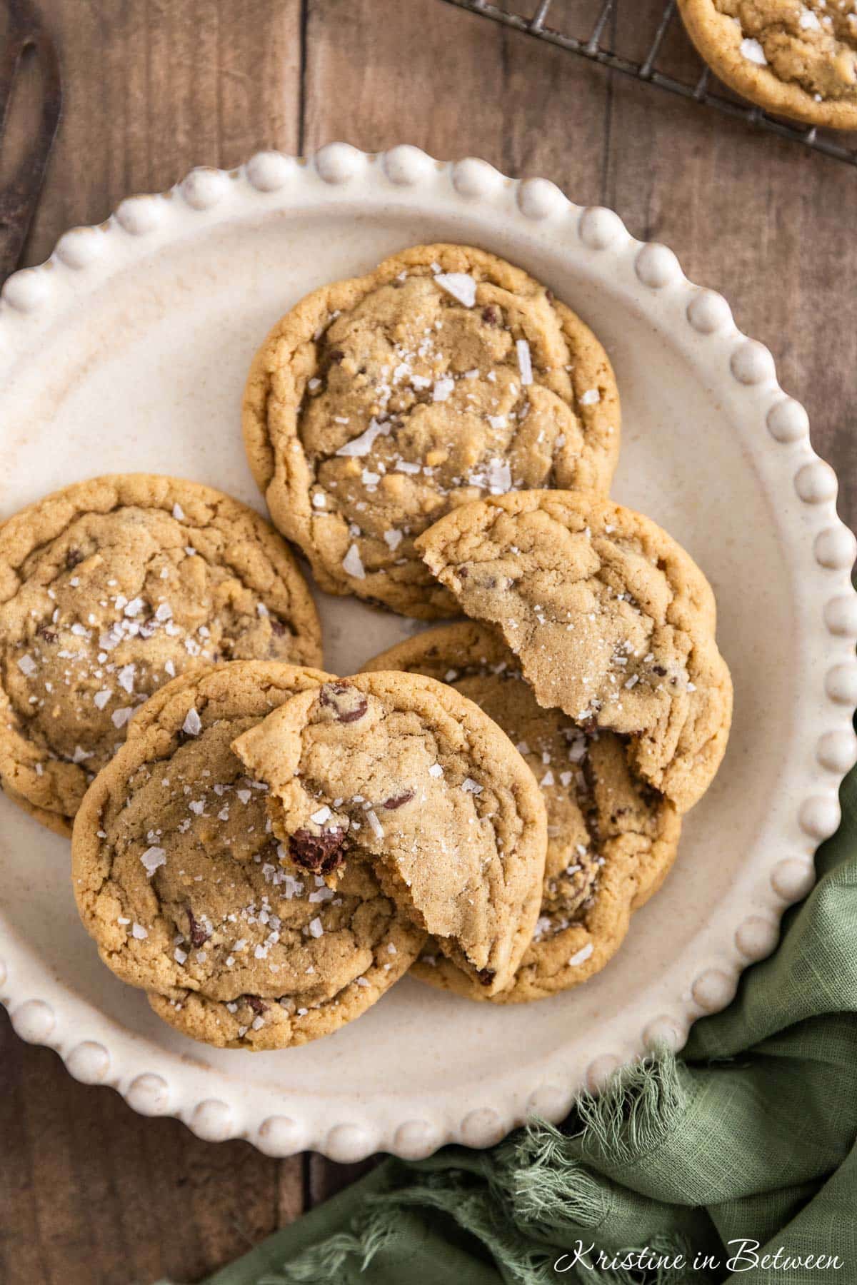 Chocolate chip cookies with sea salt sprinkled on top sitting on a white plate.