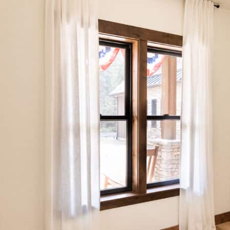 Full length curtains over a wood trimmed window, softly sitting on the floor.