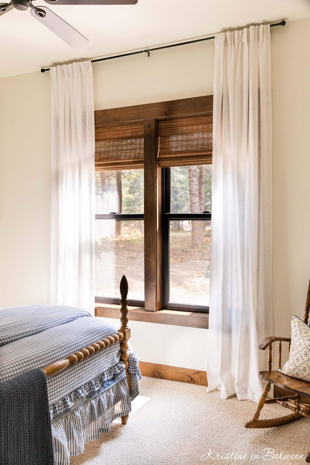A bedroom with bamboo shades and white linen drapes over the window.