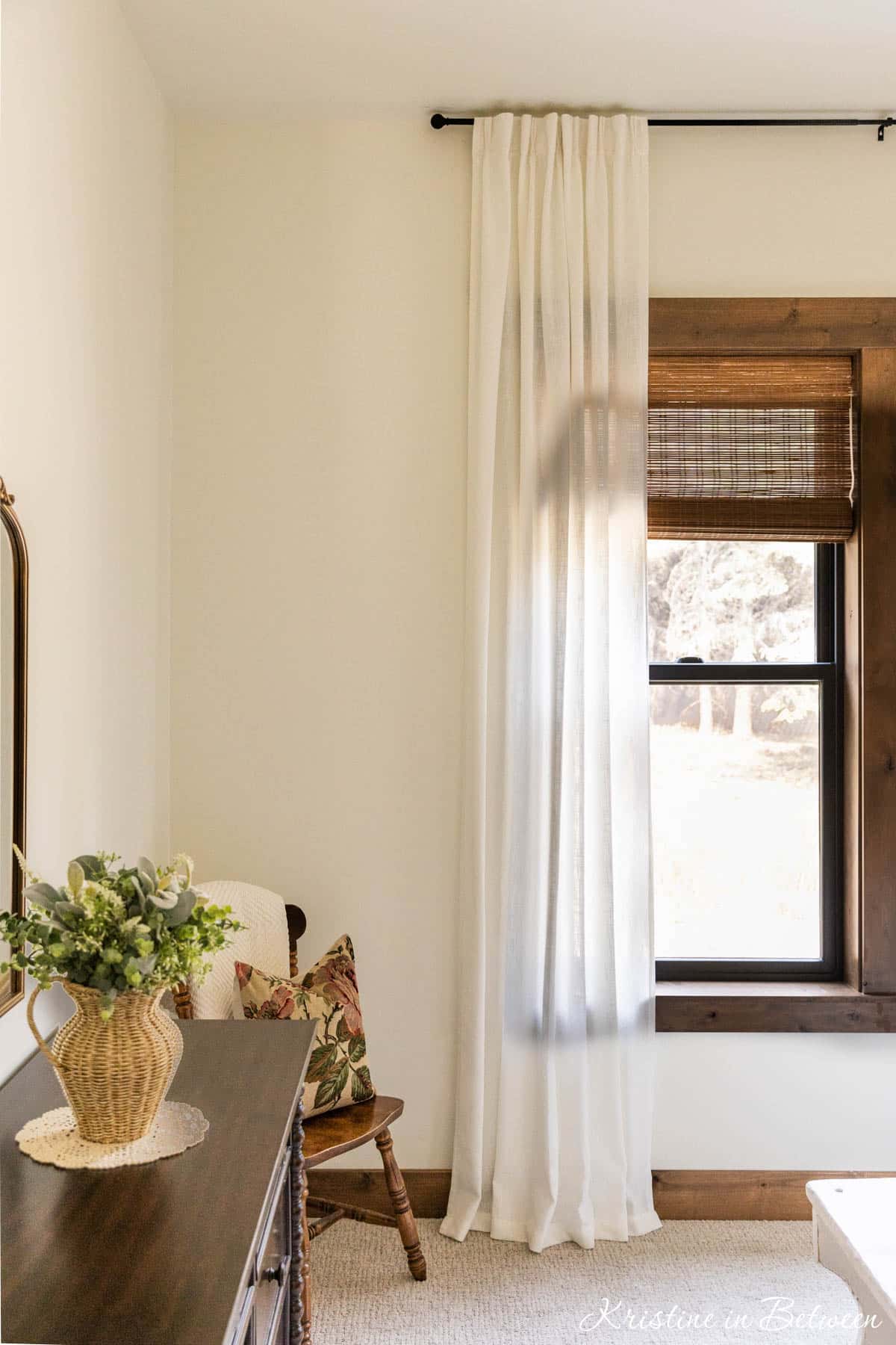 A white linen curtain hanging over an open window with a dresser off to the side.