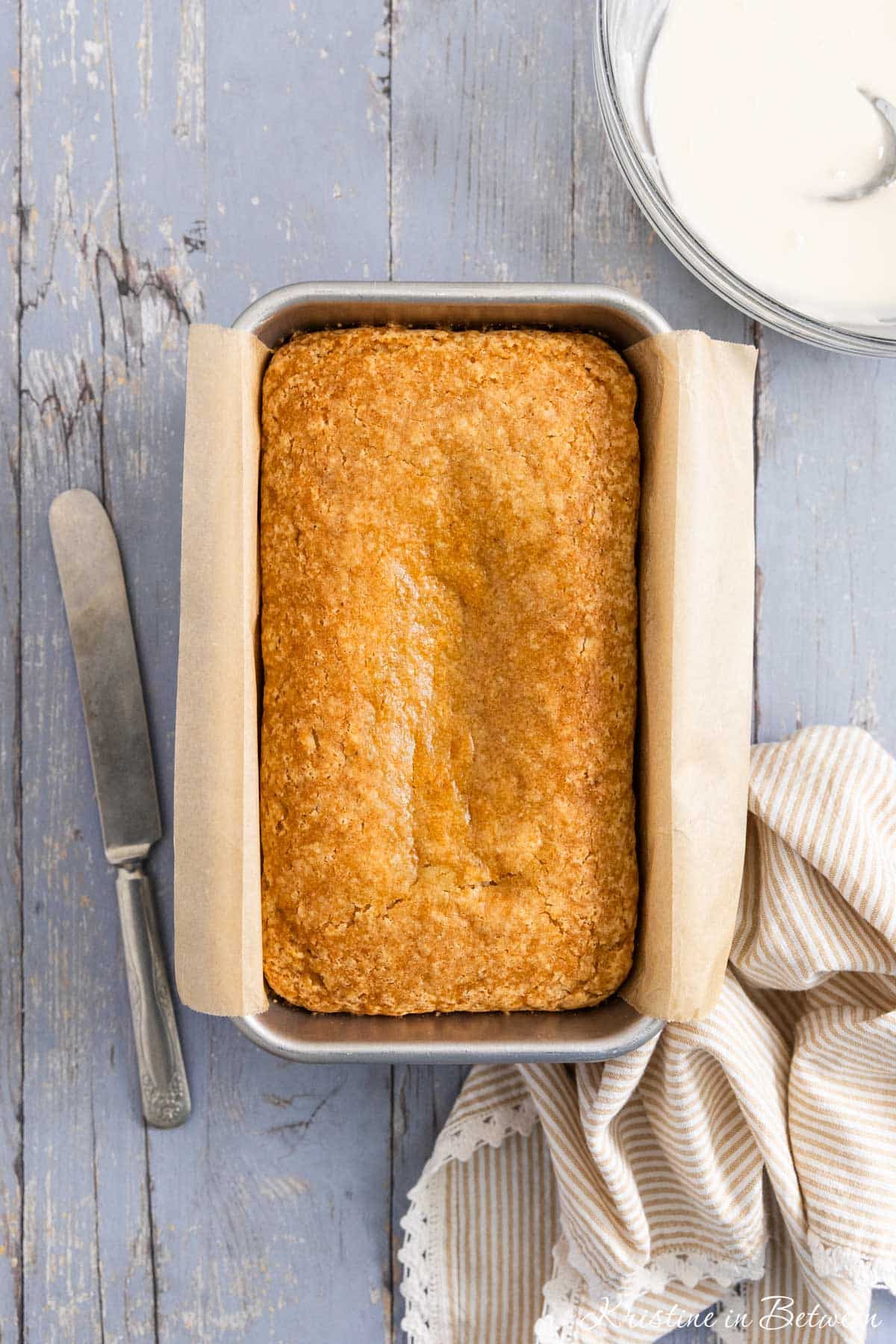 A loaf of gazed donut bread in a loaf pan with an antique knife sitting next to it.