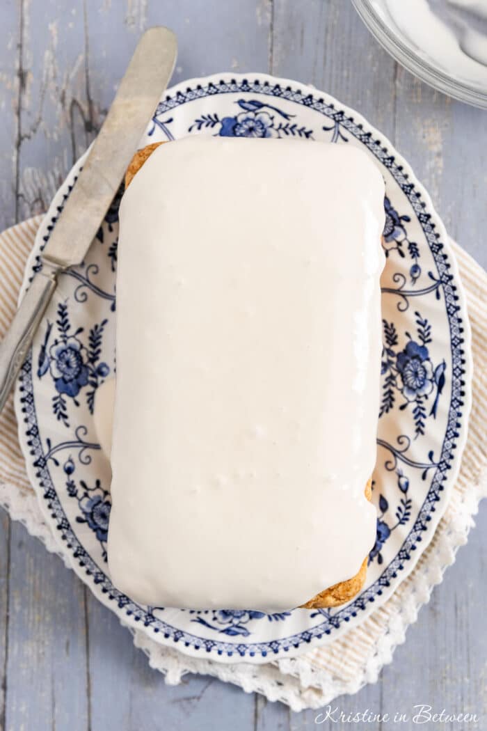 A loaf of donut bread on a platter with frosting on top and a knife sitting next to it.