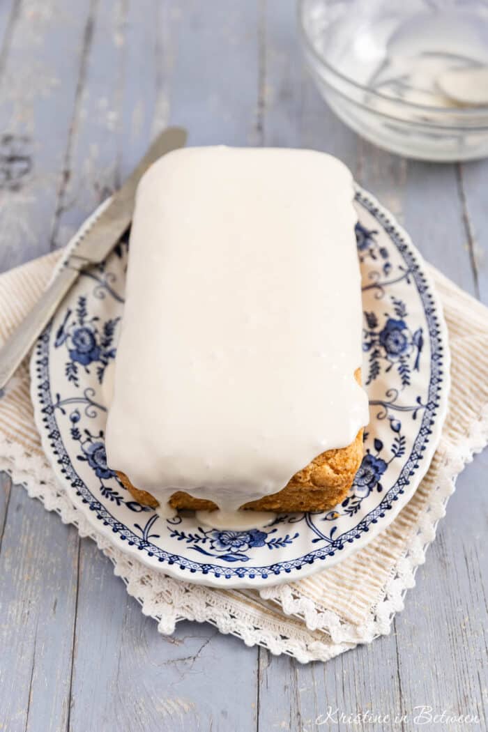 A loaf of donut bread on a platter with frosting on top and a knife sitting next to it.