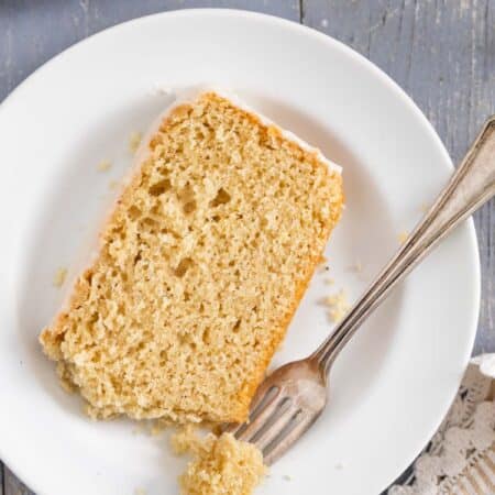 A loaf of donut bread on a platter with frosting on top and a knife sitting next to it.